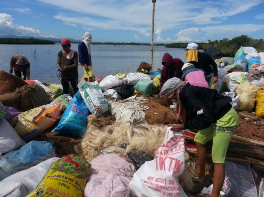 Workers are in the process of getting fibers from sacks that will be made into anti-oil spill booms to protect the mangrove areas in Day-as, Cordova.